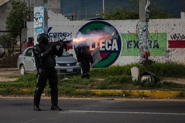 Un policía dispara su rifle durante los enfrentamientos en Oaxaca. Imagen por Manuel Velasquez/Getty Images.